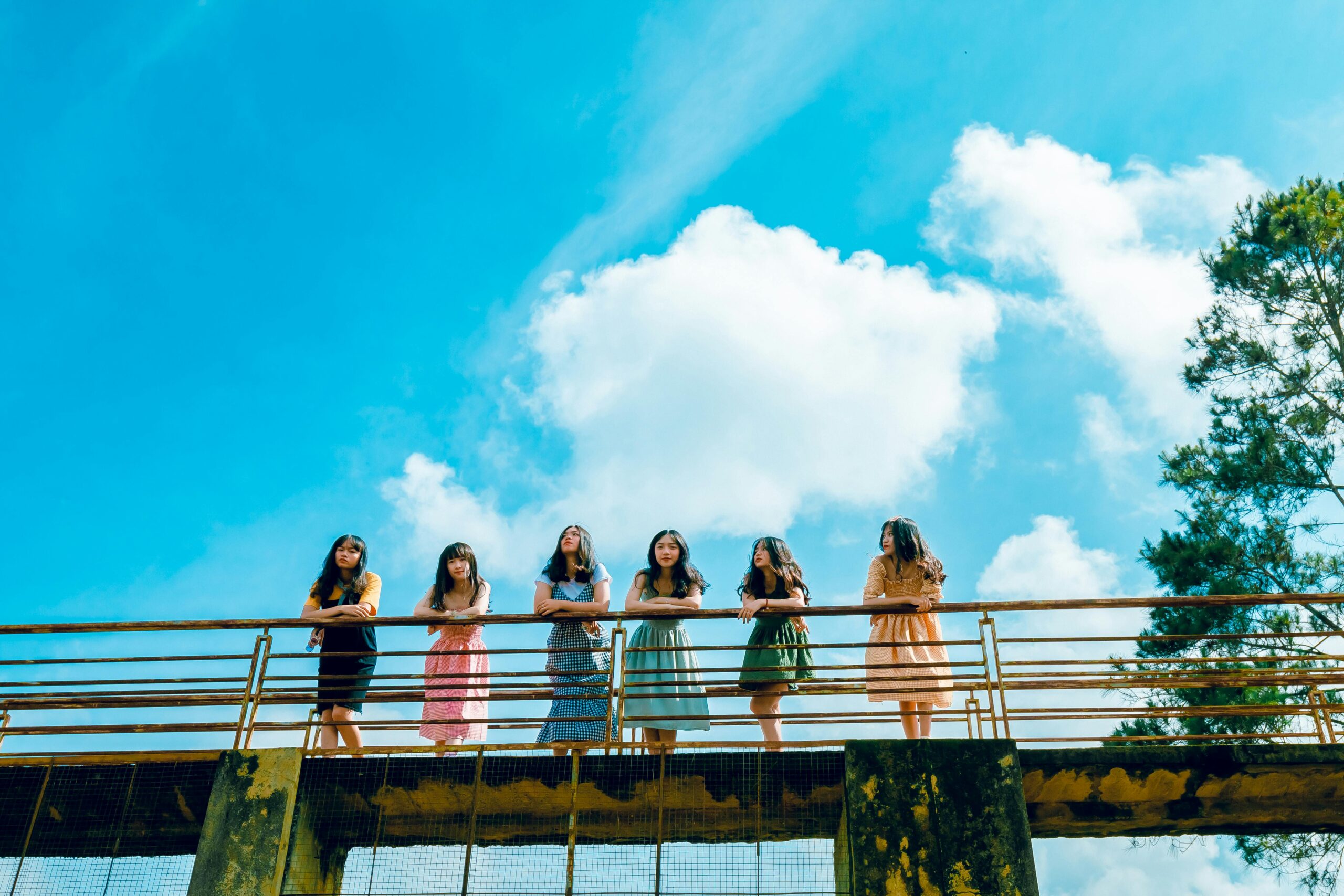 A group of young women standing on a bridge under a bright summer sky, enjoying leisure time.